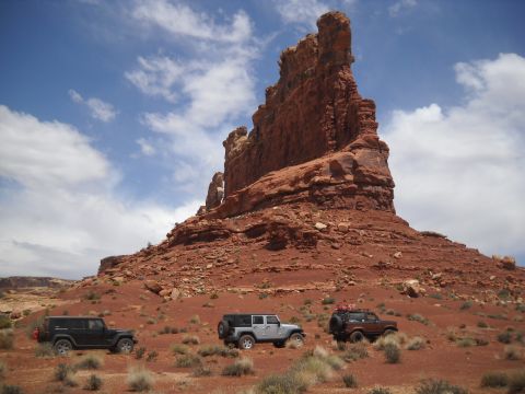 1986 Ford Bronco II - Three SUVs are parked in a desert landscape with a large rock formation under a cloudy sky.