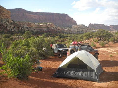 1986 Ford Bronco II - A 1986 Ford Bronco II and a Jeep are parked at a campsite in a desert canyon, with a tent set up in the foreground.
