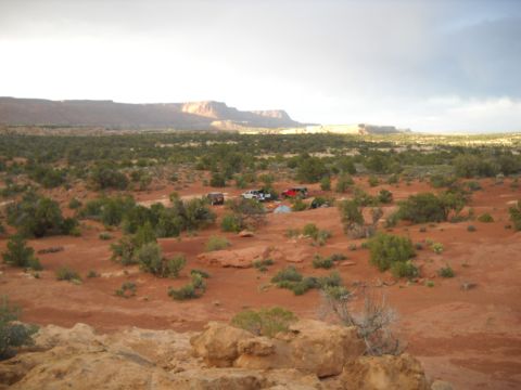 1986 Ford Bronco II - Several vehicles and tents are set up in a desert landscape with mesas in the background.