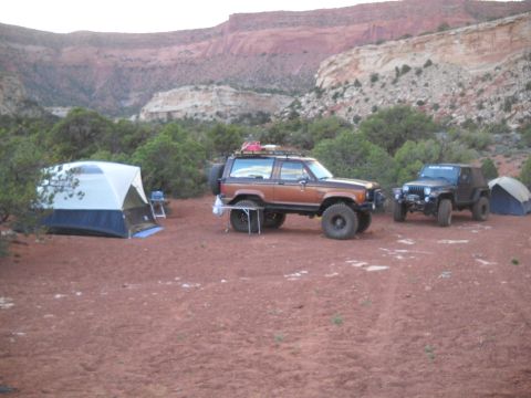 1986 Ford Bronco II - Two off-road vehicles are parked at a campsite in a desert landscape with tents set up.