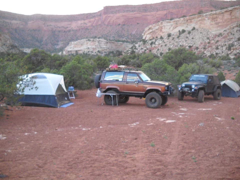 Brown Ford Bronco II and black Jeep Wrangler parked at a campsite with tents and red rock formations in the background