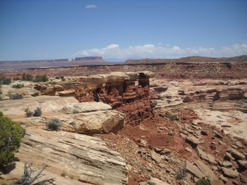 1986 Ford Bronco II - A vast desert landscape features layered red rock formations and sparse vegetation under a clear blue sky.