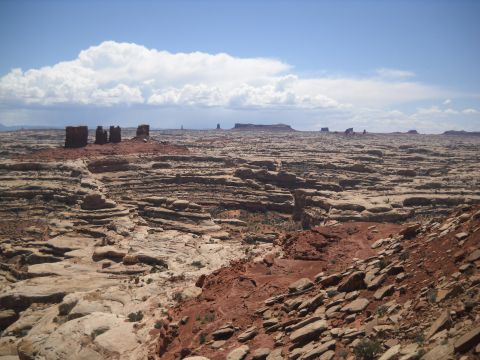 1986 Ford Bronco II - A vast desert landscape unfolds under a partly cloudy sky, layered rock formations and distant mesas.