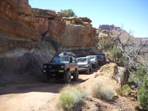 1986 Ford Bronco II - A convoy of off-road vehicles navigates a rocky canyon trail under a clear blue sky.