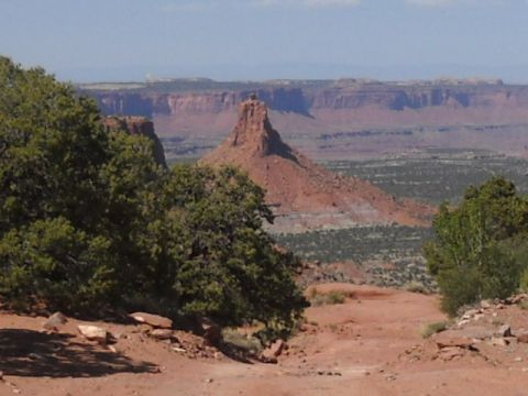 1986 Ford Bronco II - A vast desert landscape unfolds with towering red rock formations and scattered vegetation under a clear blue sky.