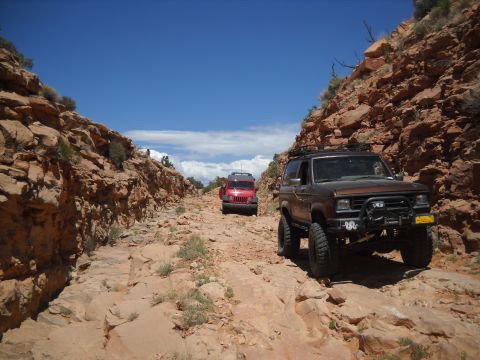 1986 Ford Bronco II - Two SUVs navigate a , rocky canyon trail under a bright blue sky.