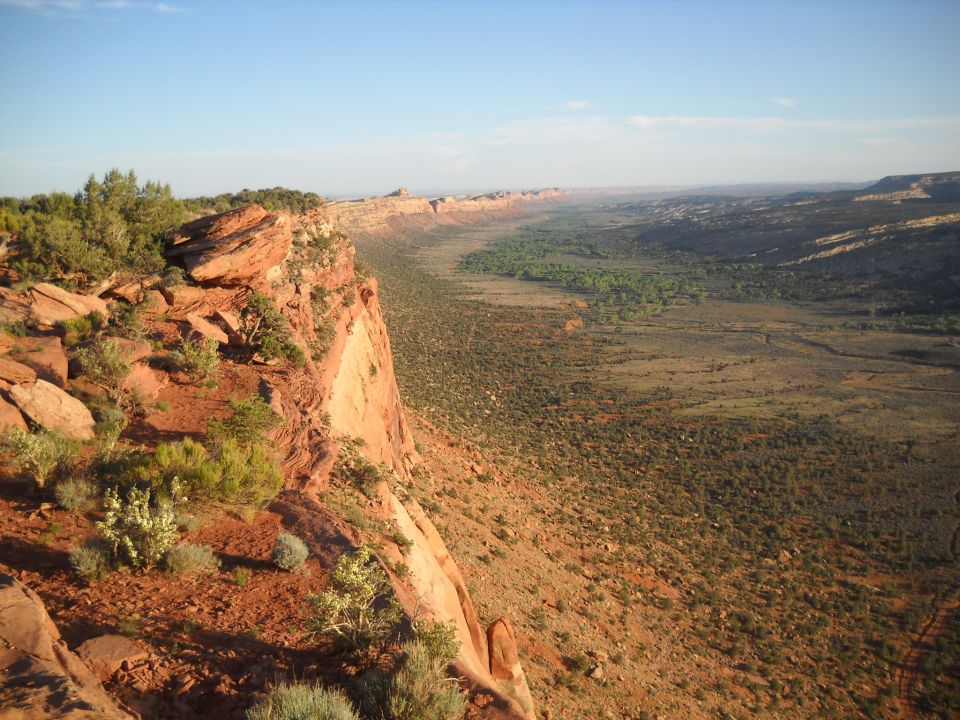 Canyon landscape with red rock cliffs and a wide valley under a clear blue sky