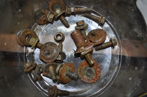 1986 Ford Bronco - A collection of heavily rusted bolts and washers are shown in a clear container, likely removed during a restoration project.