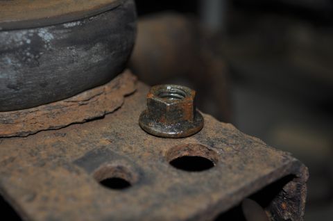 1986 Ford Bronco - A close-up view of a rusted nut secured to a metal bracket, suggesting a part of a vehicle's undercarriage.