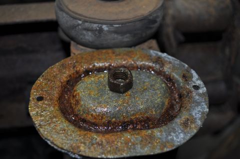 1986 Ford Bronco - Close-up of a heavily rusted metal component with a nut, likely from a vehicle's undercarriage.