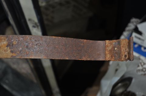 1986 Ford Bronco - Close-up of a heavily rusted metal strap, possibly a vehicle part, with 'SUPERMOTORS' visible in the background.