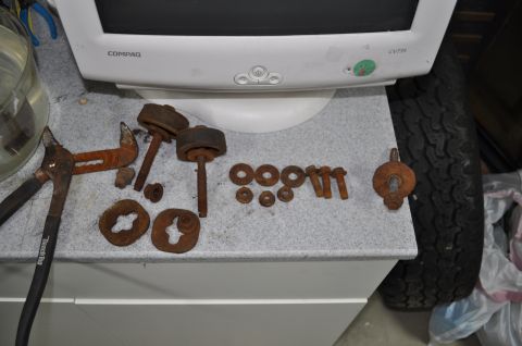 1986 Ford Bronco - Assorted rusty automotive parts and tools are displayed on a workbench surface.