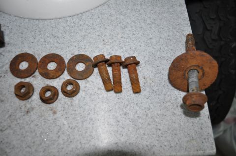 1986 Ford Bronco - A collection of heavily rusted bolts and washers are laid out on a speckled surface next to a tire.