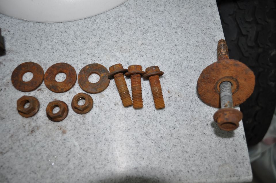 Rusty bolts and washers on a speckled surface, with a tire visible on the right