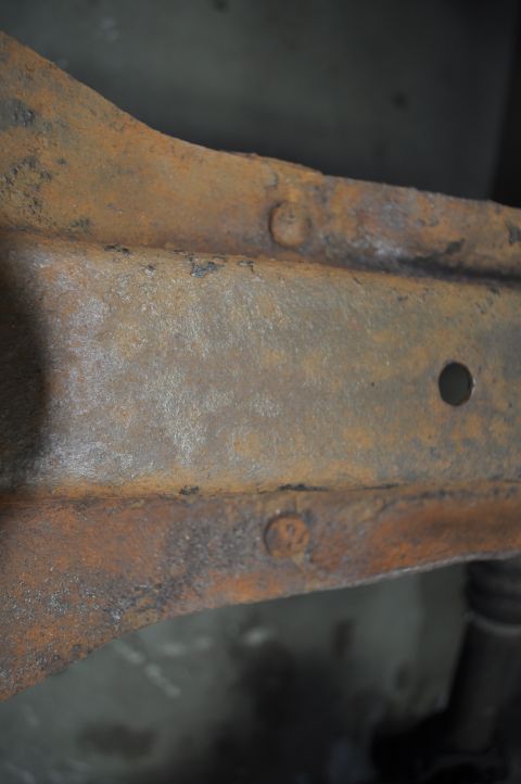 1986 Ford Bronco - Close-up view of a heavily rusted vehicle frame, showing structural components and fasteners.