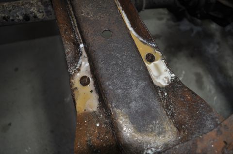 1986 Ford Bronco - A close-up view of a heavily rusted metal frame part with visible residue and bolt holes.
