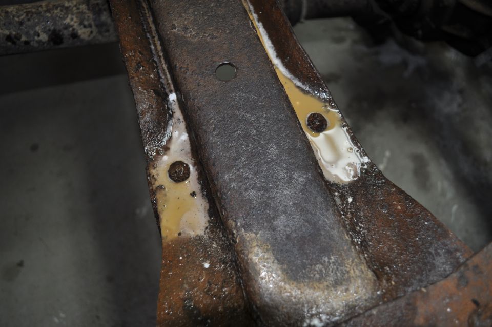 Close-up of rusted metal frame with yellow and white residue, showing bolt holes