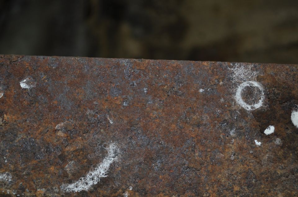 Close-up of a heavily rusted metal surface with some white residue and a circular mark