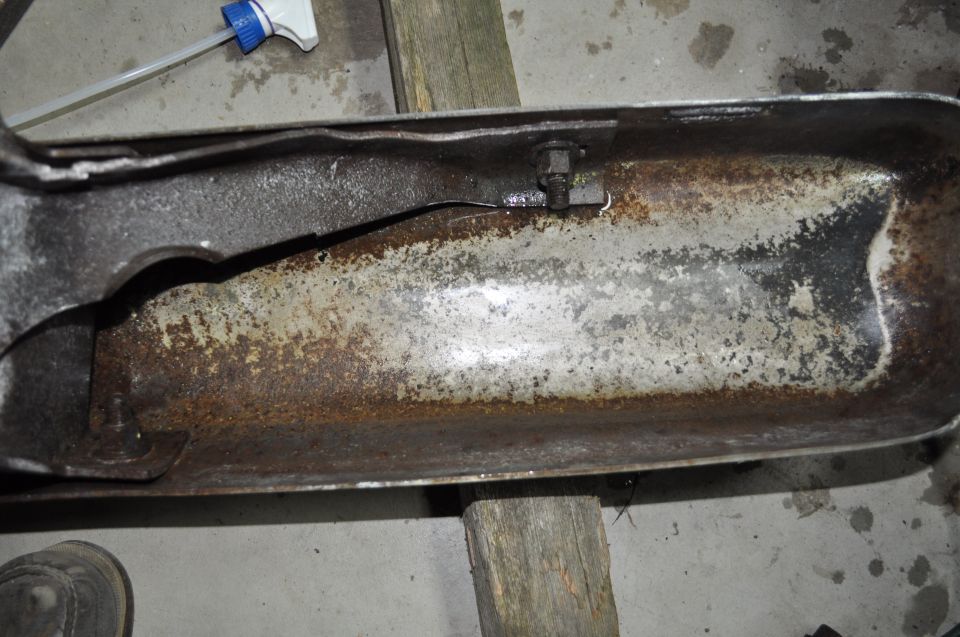 Rusted metal part with a crack, supported by wooden blocks. A spray bottle is visible in the background