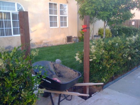 1968 Ford Mustang - Construction materials, including a wheelbarrow and wooden posts, are staged in a residential yard with a manicured lawn and hedges.