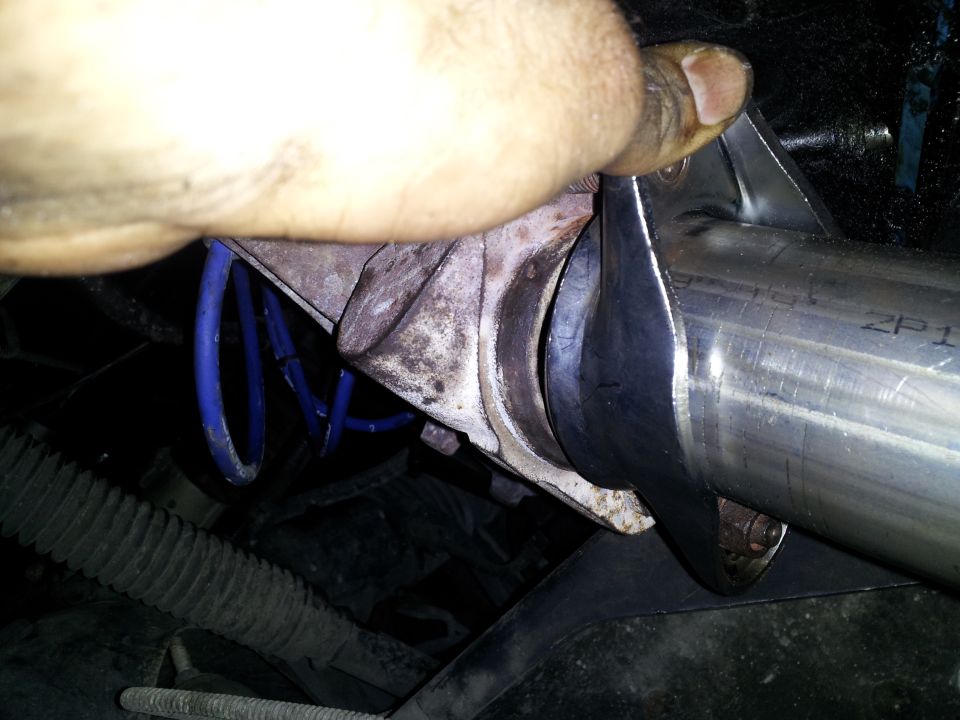 Close-up of a metal exhaust pipe being worked on, with a blue suspension spring visible