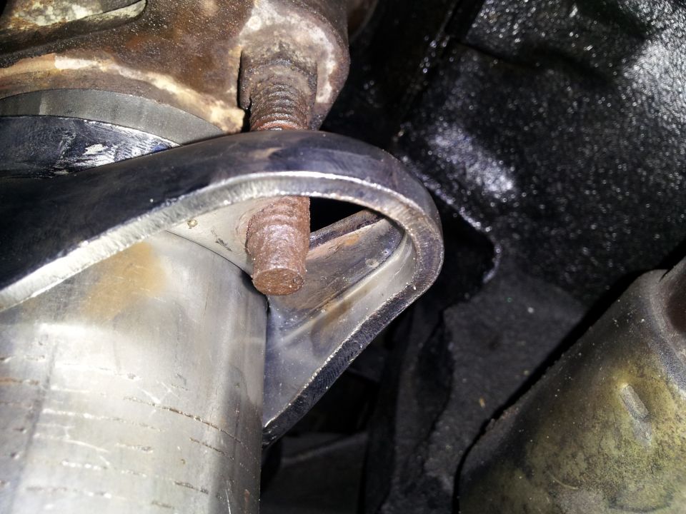 Rusty exhaust stud without a nut protruding through a stainless exhaust bracket under a vehicle