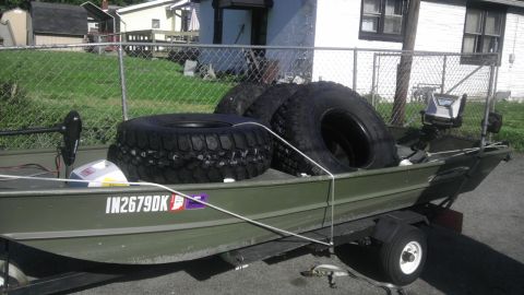 1989 Ford Bronco - A green boat on a trailer carries four large tires, with a trolling motor visible at the front.