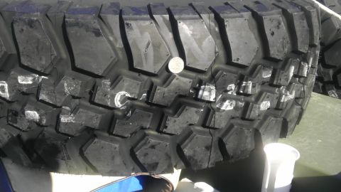 1989 Ford Bronco - A close-up view of an off-road tire, showing its aggressive tread pattern and a coin placed on top.