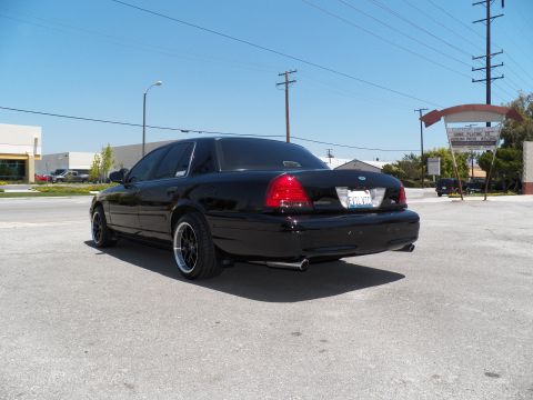 2003 Ford Crown Victoria - Black Crown Victoria photographed outside in a lot, showing lowered stance, dual exhaust and dark wheels.