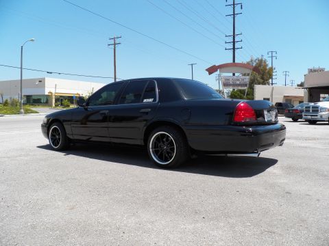 2003 Ford Crown Victoria - Rear quarter of a blacked-out Crown Victoria on black wheels, parked outside an industrial building.