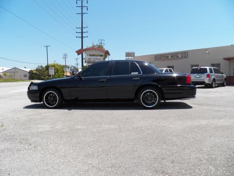 2003 Ford Crown Victoria - Side profile of a lowered black sedan on staggered black wheels against a warehouse backdrop.