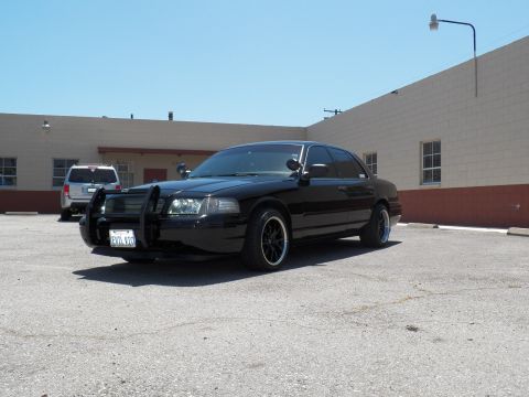 2003 Ford Crown Victoria - Lowered black sedan with grille guard and California plate, parked beside a building.