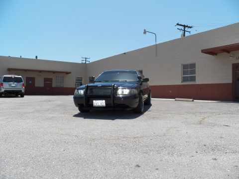 2003 Ford Crown Victoria - Front view of a black sedan with headlights lit and a push-bar grille guard.