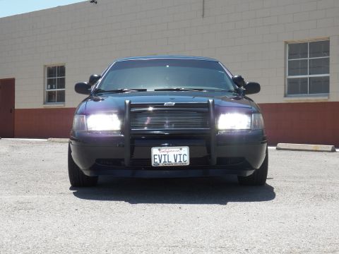 2003 Ford Crown Victoria - Front view of a black sedan with lit headlights, push bar and EVIL VIC plate.