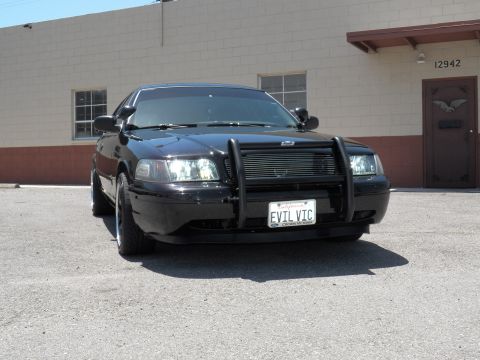 2003 Ford Crown Victoria - Black sedan with grille guard and EVIL VIC plate parked at an industrial unit.