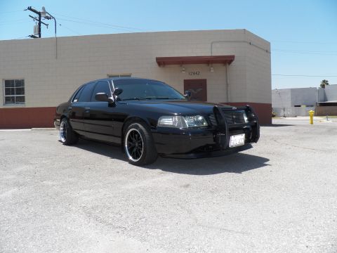 2003 Ford Crown Victoria - Lowered black sedan on staggered black wheels viewed from the front quarter.
