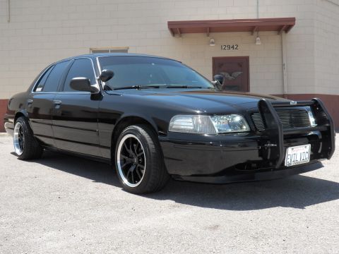 2003 Ford Crown Victoria - Lowered black sedan with EVIL VIC plate and grille guard, front quarter view.