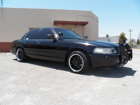 2003 Ford Crown Victoria - Front quarter of a lowered black sedan with push bar parked under clear skies.