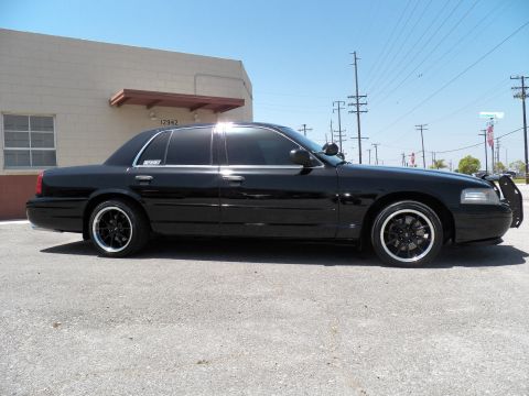 2003 Ford Crown Victoria - Side profile of a lowered black sedan on staggered black wheels by a warehouse.