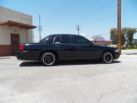 2003 Ford Crown Victoria - Passenger-side profile of a black sedan on black wheels outside a warehouse unit.