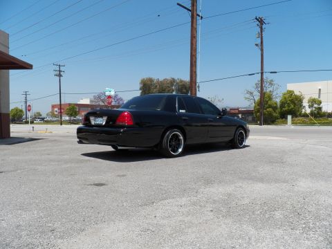2003 Ford Crown Victoria - Rear quarter view of a black sedan on black wheels parked near street signage.