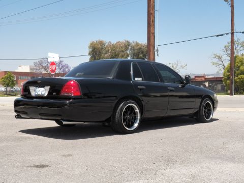 2003 Ford Crown Victoria - Rear quarter of a blacked-out Crown Victoria at the curb beside a stop sign.