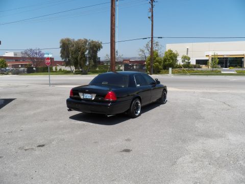 2003 Ford Crown Victoria - Distant rear quarter view of a black sedan parked across an open roadway.