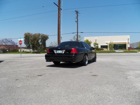 2003 Ford Crown Victoria - Rear quarter of a lowered black Crown Victoria parked across an empty lot, stop sign at left.