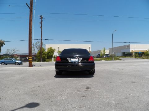 2003 Ford Crown Victoria - Black Crown Victoria seen head-on from the rear across a wide parking lot beside warehouses.
