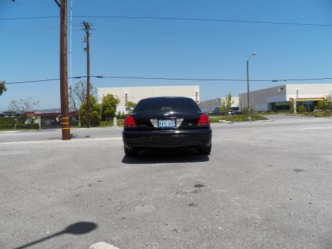 2003 Ford Crown Victoria - Distant rear shot of a black Crown Victoria in a large lot with a warehouse behind it.