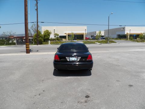 2003 Ford Crown Victoria - Black Crown Victoria photographed from behind across a roadway in front of industrial buildings.