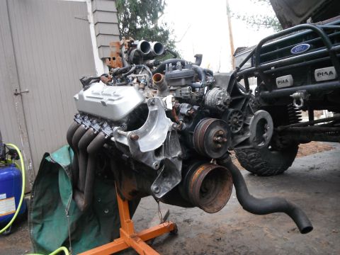 1988 Ford Bronco - Engine on a stand is positioned next to the front end of a Ford Bronco.