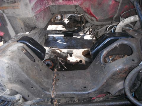 1988 Ford Bronco - Underside view of a vehicle frame showing engine mounts and drivetrain components, with another vehicle visible in the background.