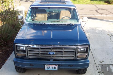 1980 Ford Bronco - This blue Ford van, likely from the 1980s, is shown from the front with its grille and license plate clearly visible.